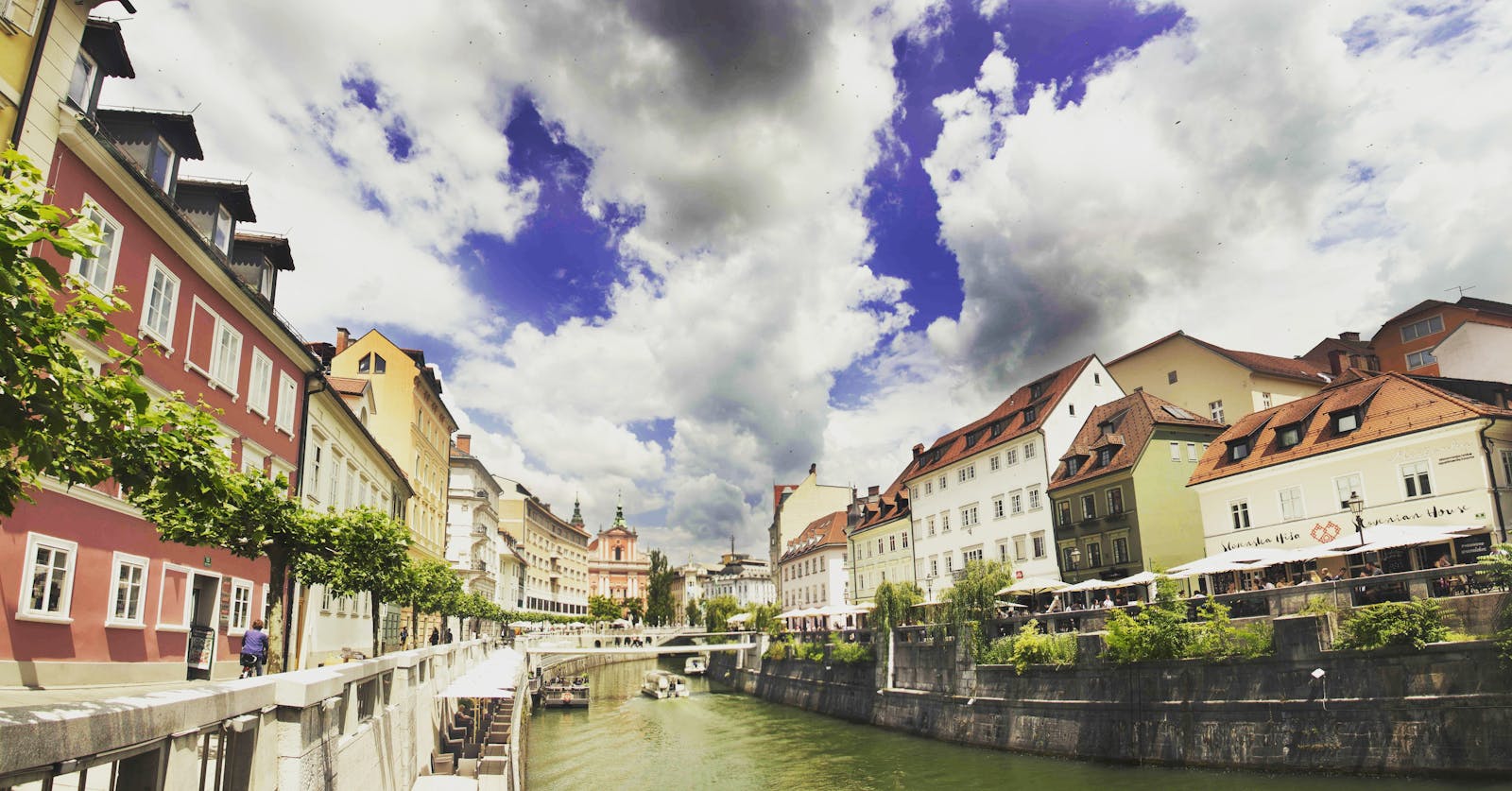 Scenic view of colorful riverside buildings in Ljubljana, showcasing vibrant architecture under dramatic skies.